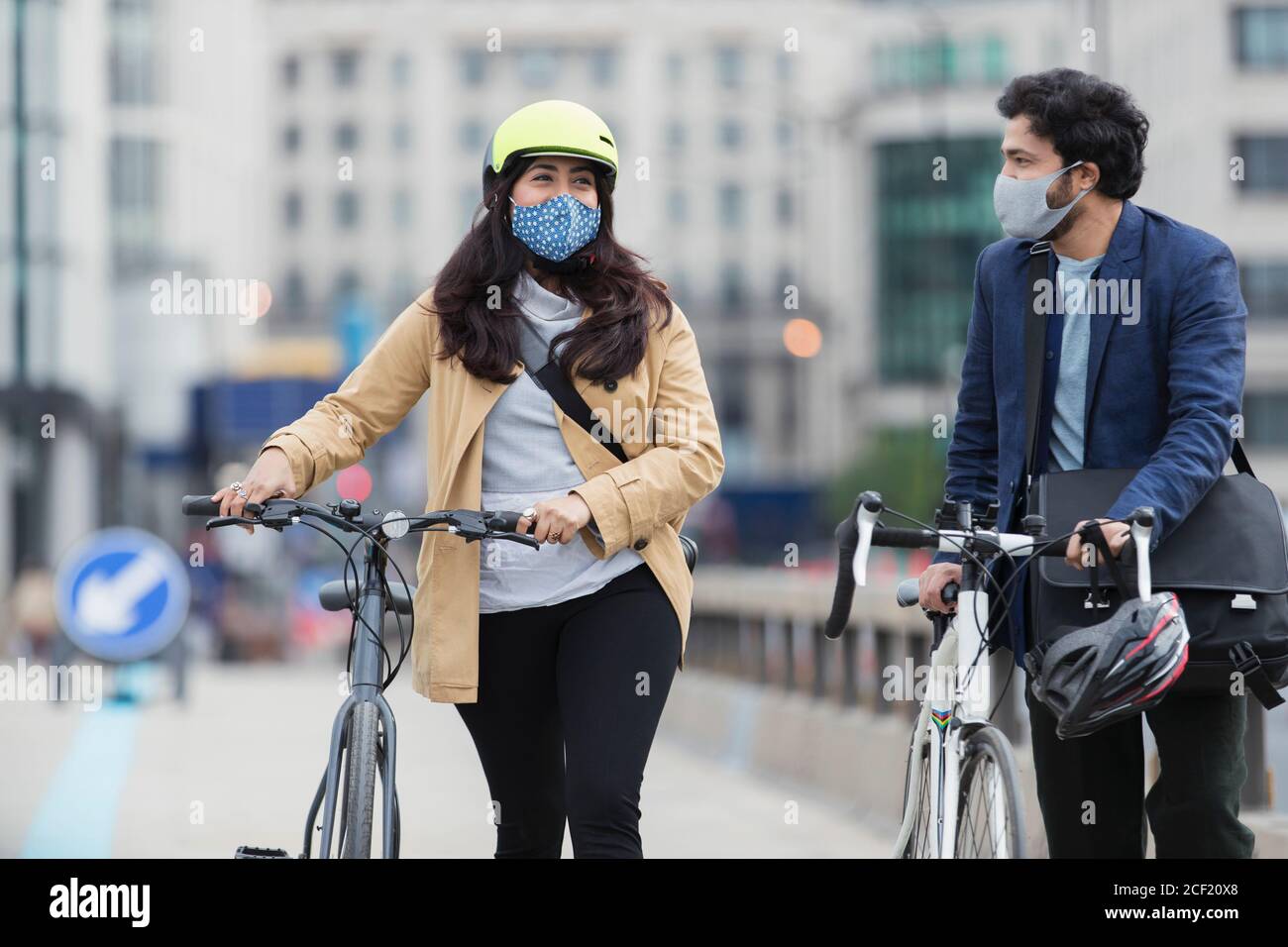 Business people in face masks walking bicycles on city  bridge Stock Photo