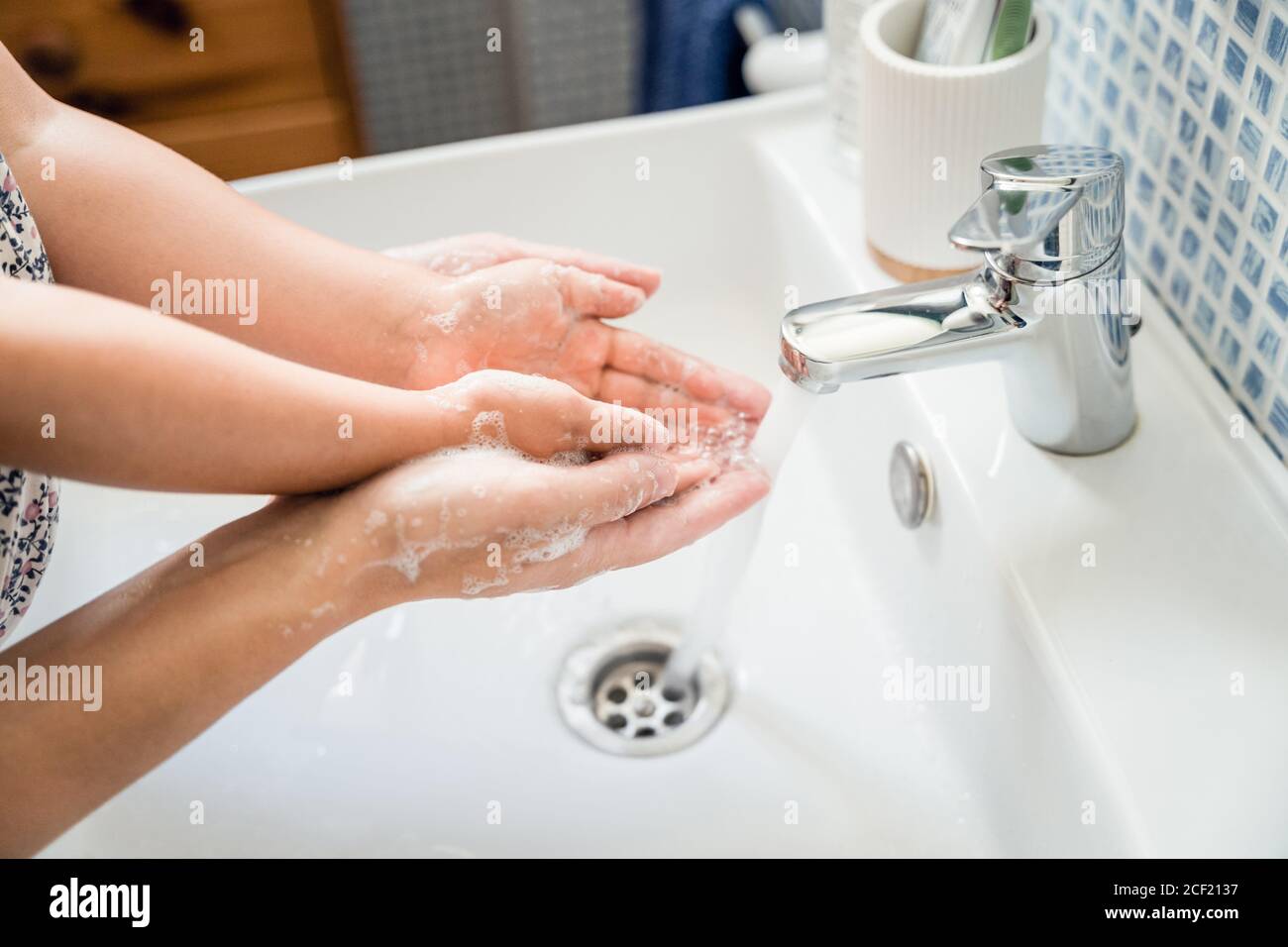 Mother and girl child washing hands together in bathroom sink with soap under running water tap to rinse off. Fingers hands extended open. High point Stock Photo