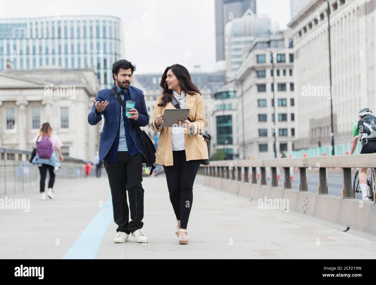 Business people with coffee and digital tablet talking on city bridge Stock Photo