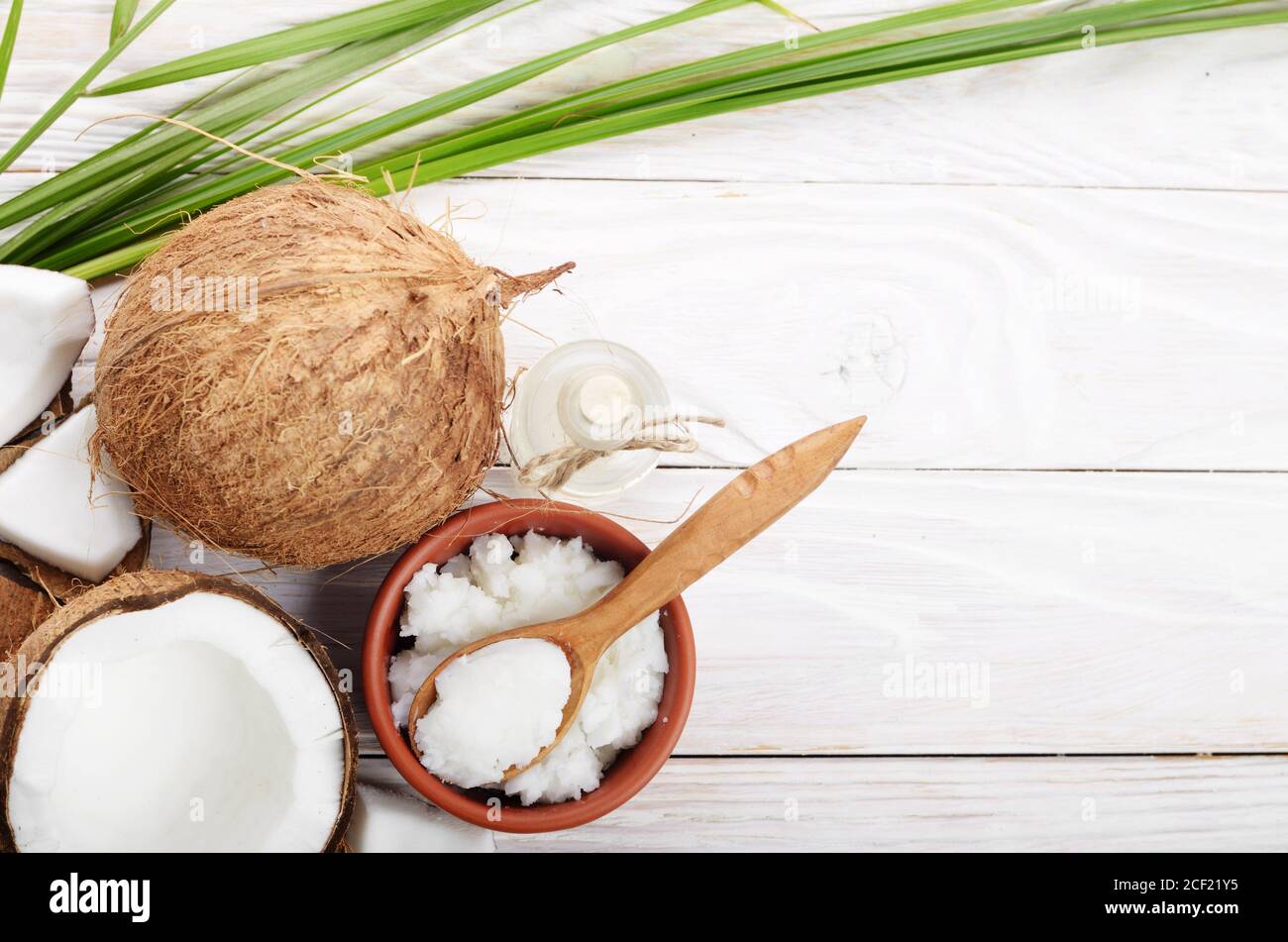 Flat lay Background of coconut, coconut shell, oil in clay bowl and glass jar and spoon on white wooden table. Stock Photo