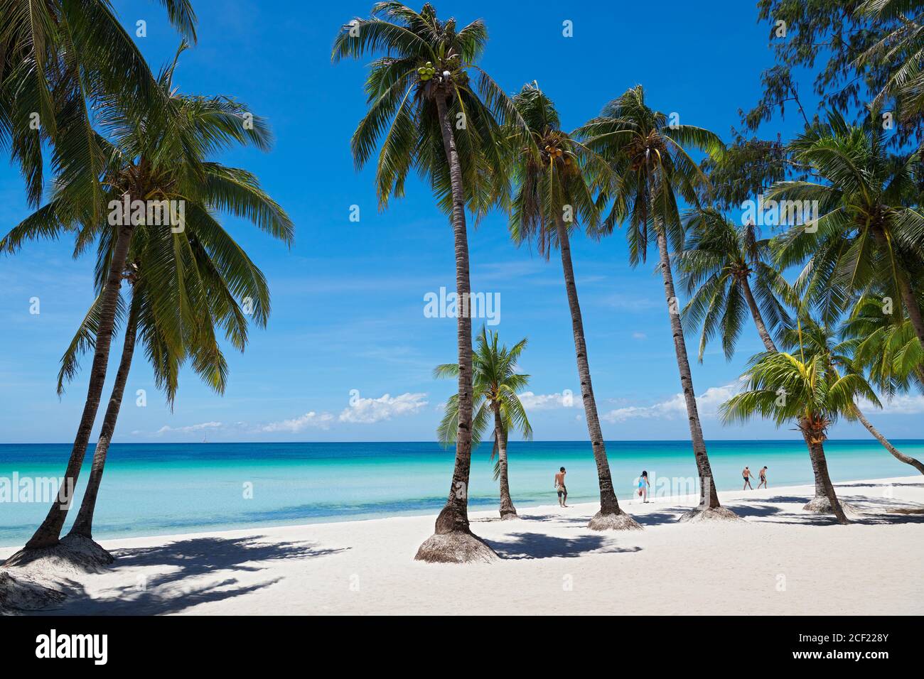 A group of people walking next to coconut trees along the clean White Beach of Boracay Island, Aklan, Visayas, Philippines, at a sunny day. Stock Photo