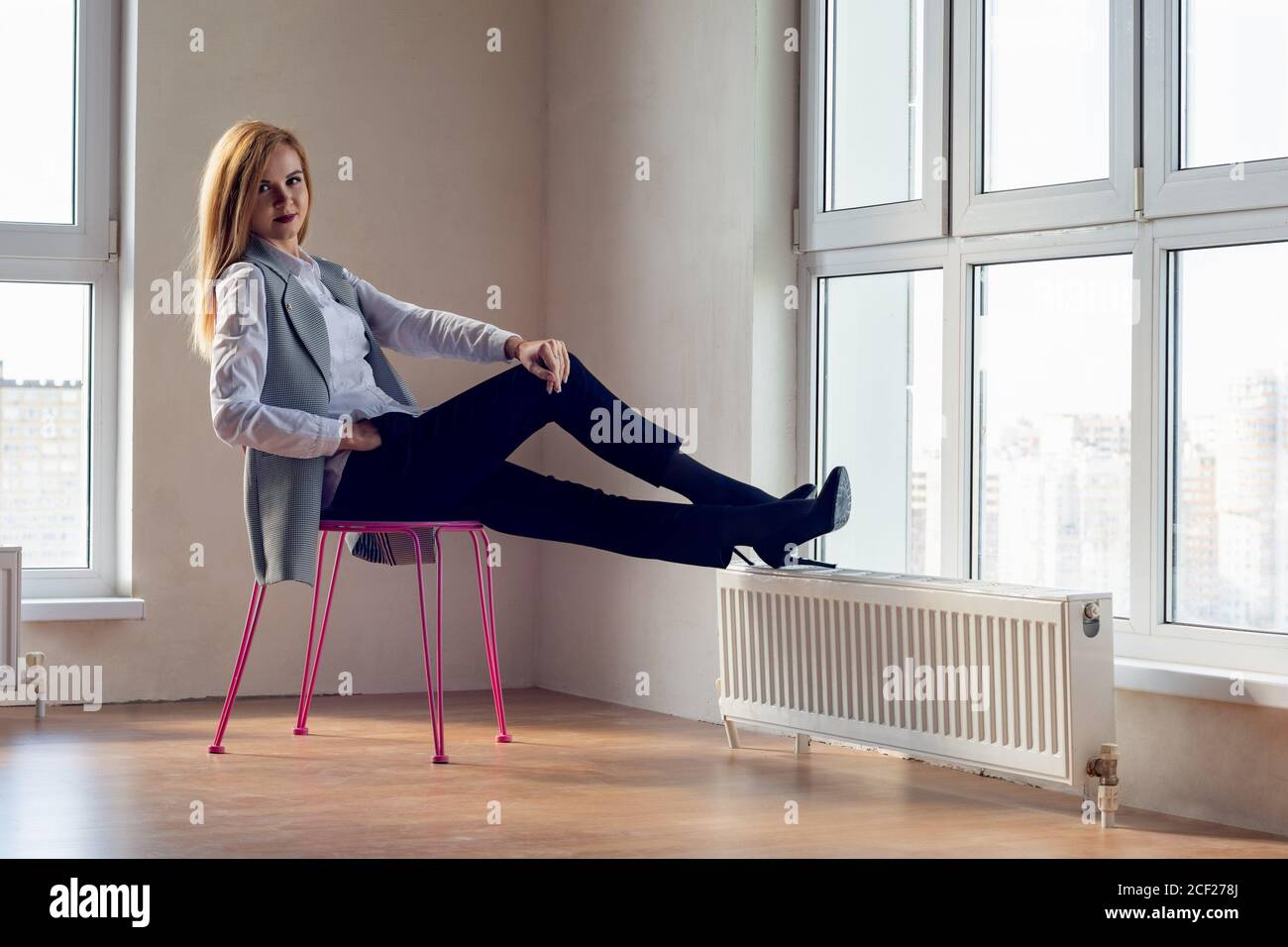 elegant girl in uninhibited pose sits on a chair in a large empty room. Stock Photo