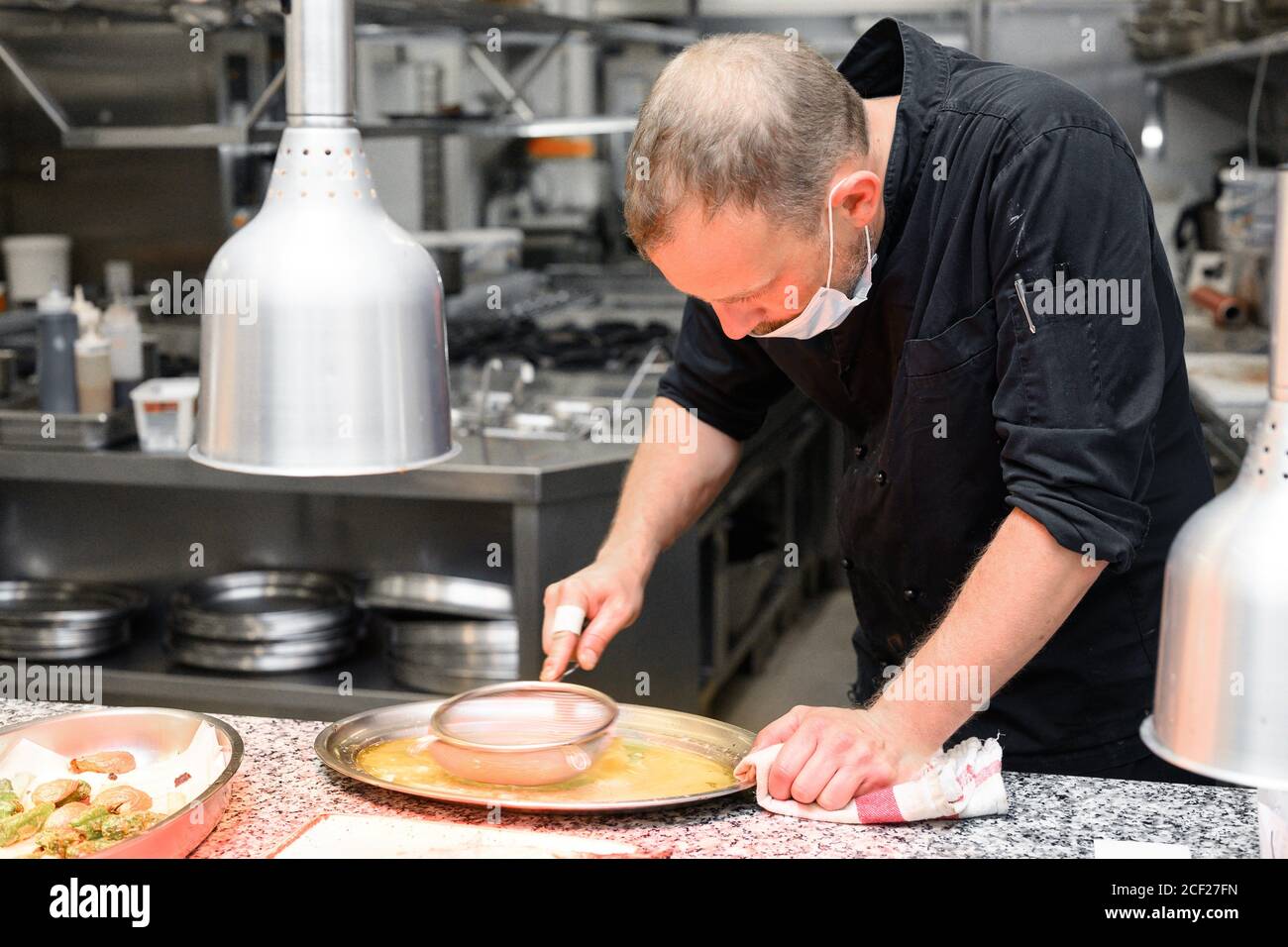 Chef in uniform cooking in a commercial kitchen. Male cook standing by kitchen counter preparing food. High quality photo. Stock Photo