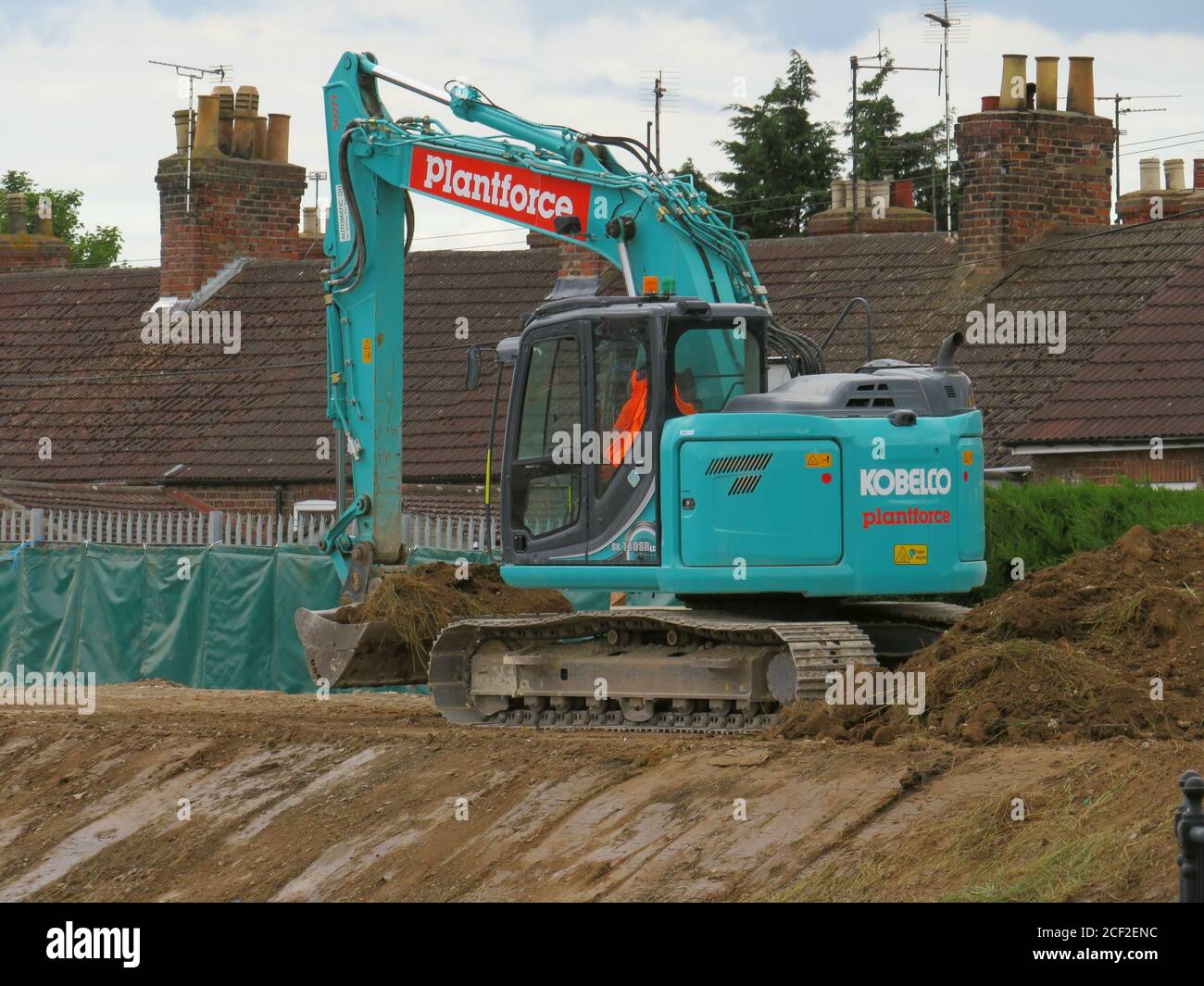 KOBELCO plantforce digger moving earth on the riverbank to shore up flood defences.opposite the new flood barrier Stock Photo