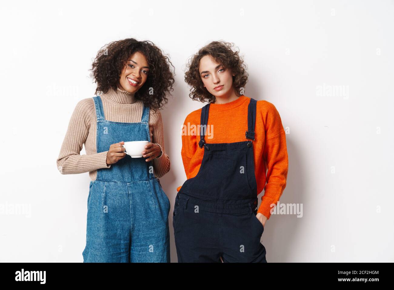 Portrait of two multinational women in overalls looking at camera and ...