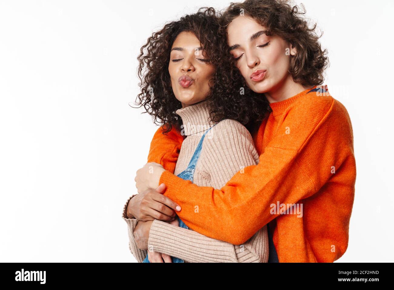 Portrait of cute multinational women in overalls making kiss lips and ...