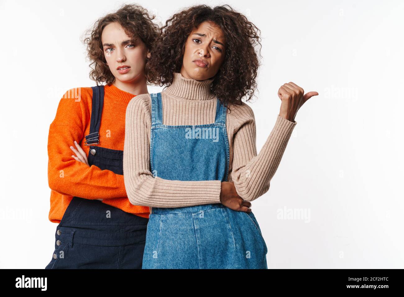 Portrait of perplexed multinational women in overalls looking at camera ...