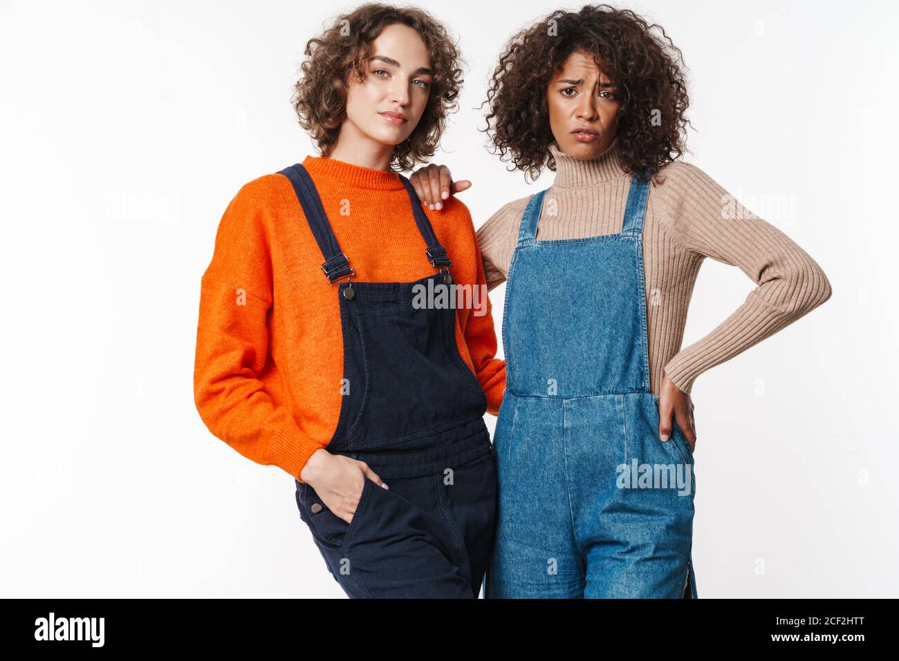 Portrait of confused multinational women in overalls looking at camera ...