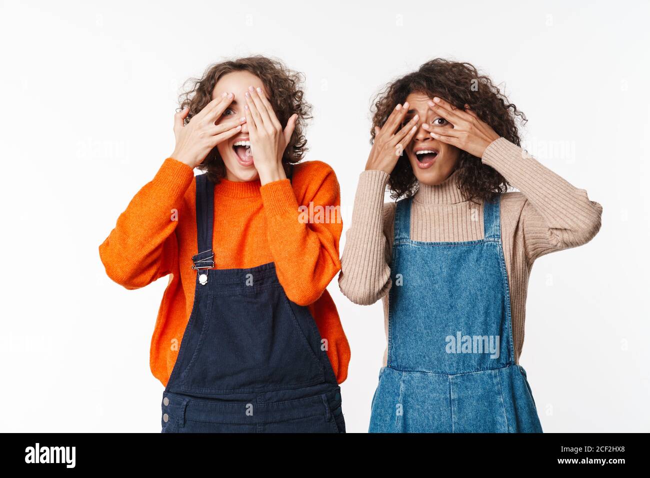 Portrait of funny multinational women in overalls covering their eyes ...