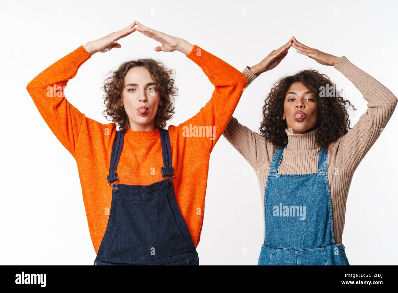 Portrait of funny multinational women in overalls making roof above ...