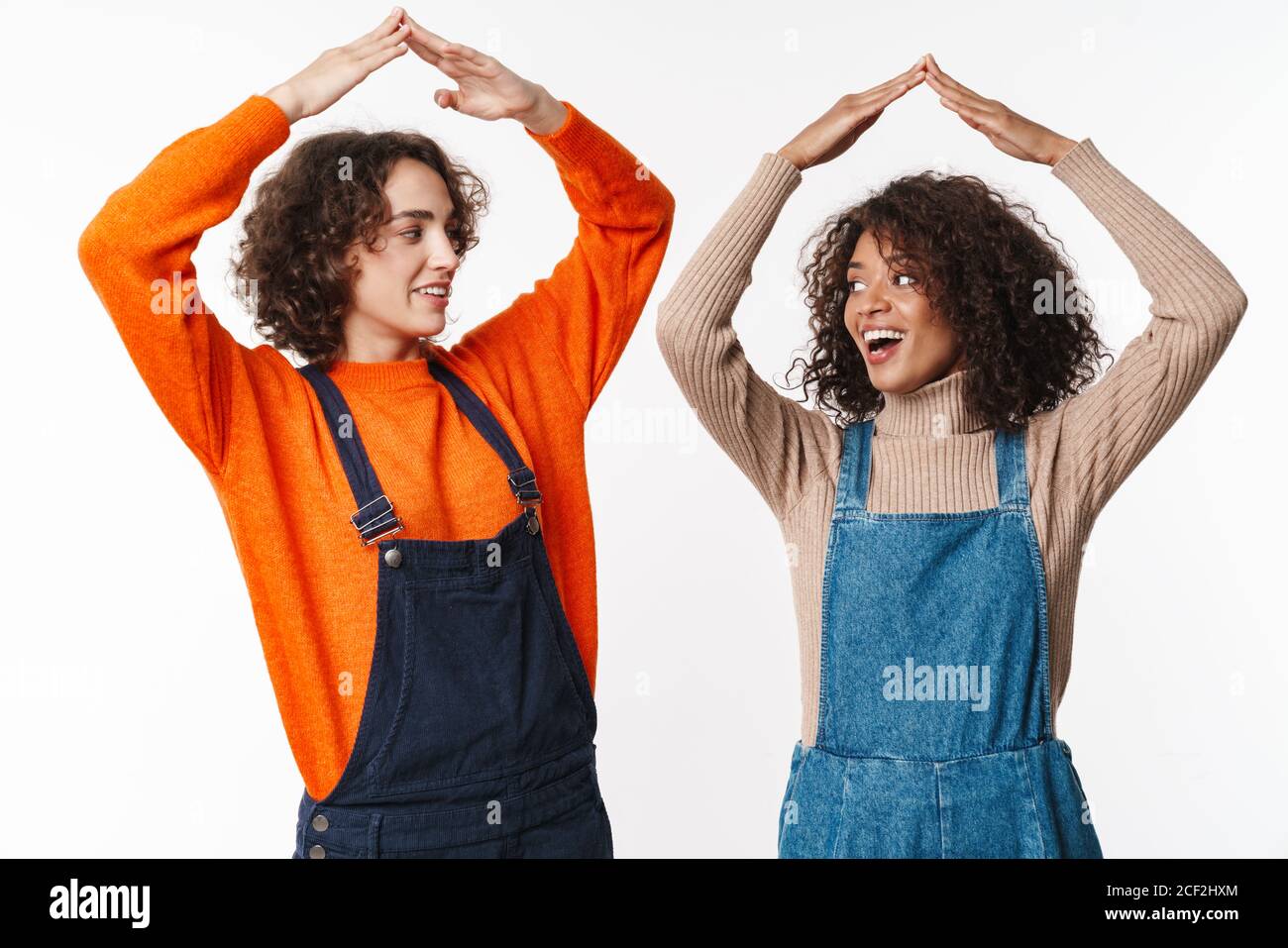 Portrait of joyful multinational women in overalls making roof above ...