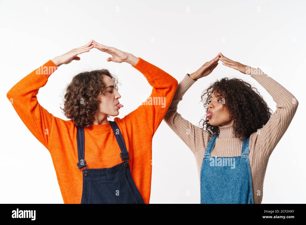 Portrait of funny multinational women in overalls making roof above ...
