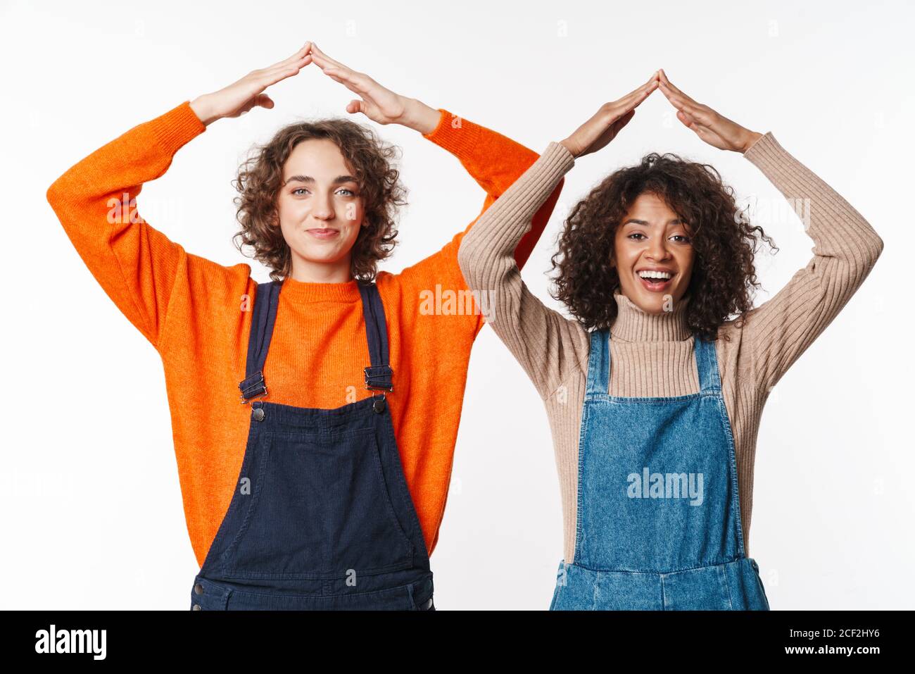 Portrait of funny multinational women in overalls making roof above ...