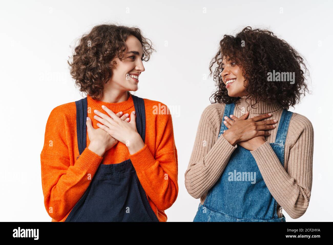 Portrait of lovely multinational women in overalls smiling and holding ...