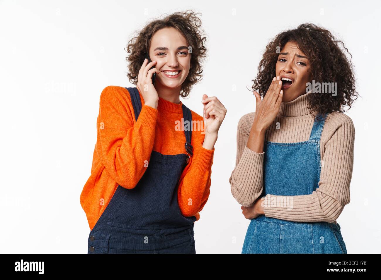Portrait of beautiful multinational women in overalls using cellphone ...