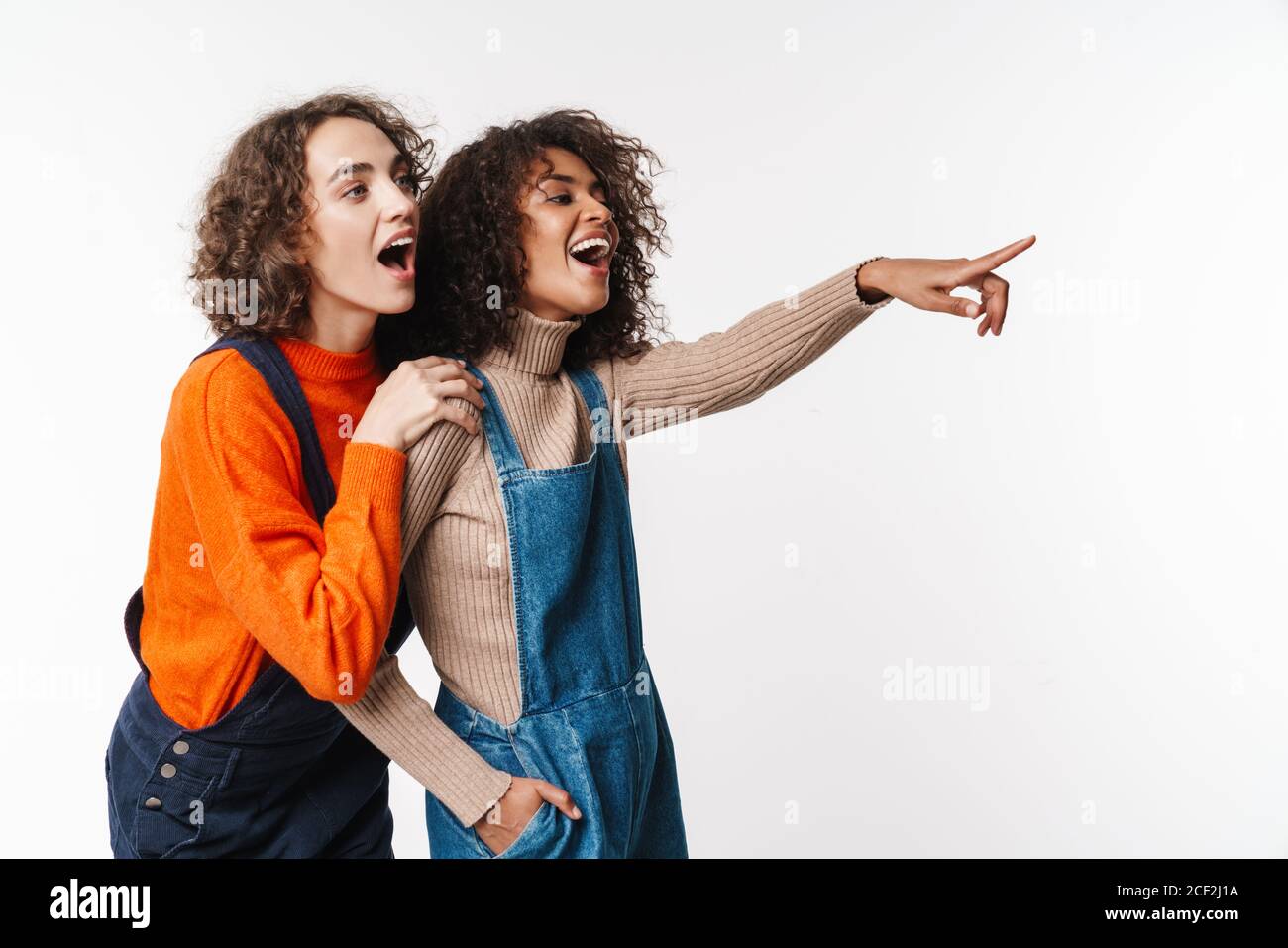Portrait of surprised multinational women in overalls pointing fingers ...