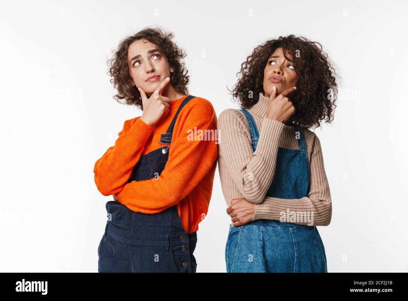 Portrait of perplexed multinational women in overalls thinking and ...