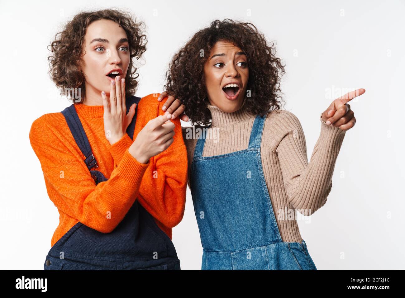 Portrait of excited multinational women in overalls pointing fingers ...