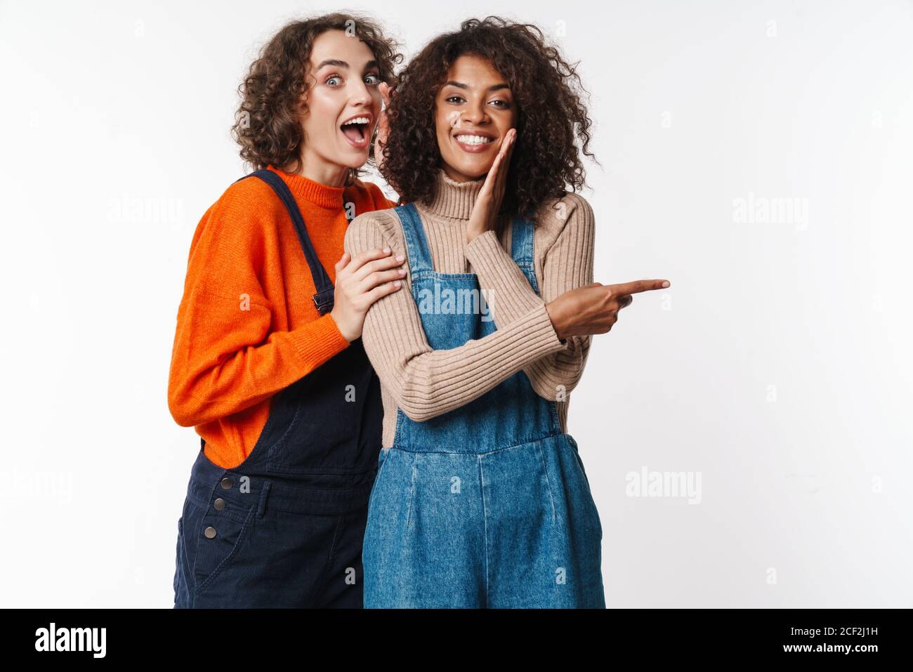 Portrait of surprised multinational women in overalls pointing finger ...