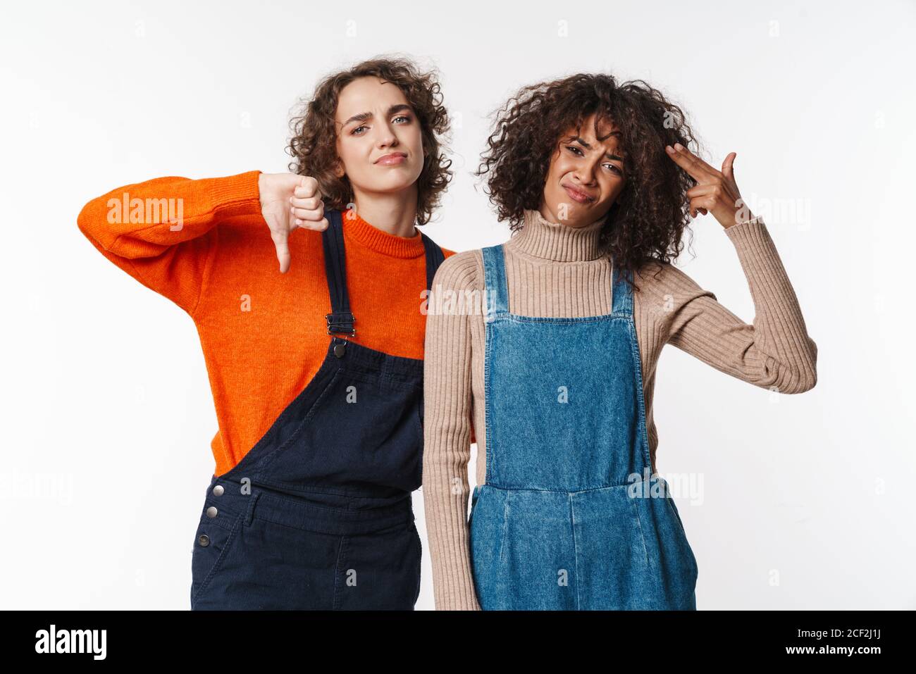 Portrait of displeased multinational women in overalls showing thumb ...