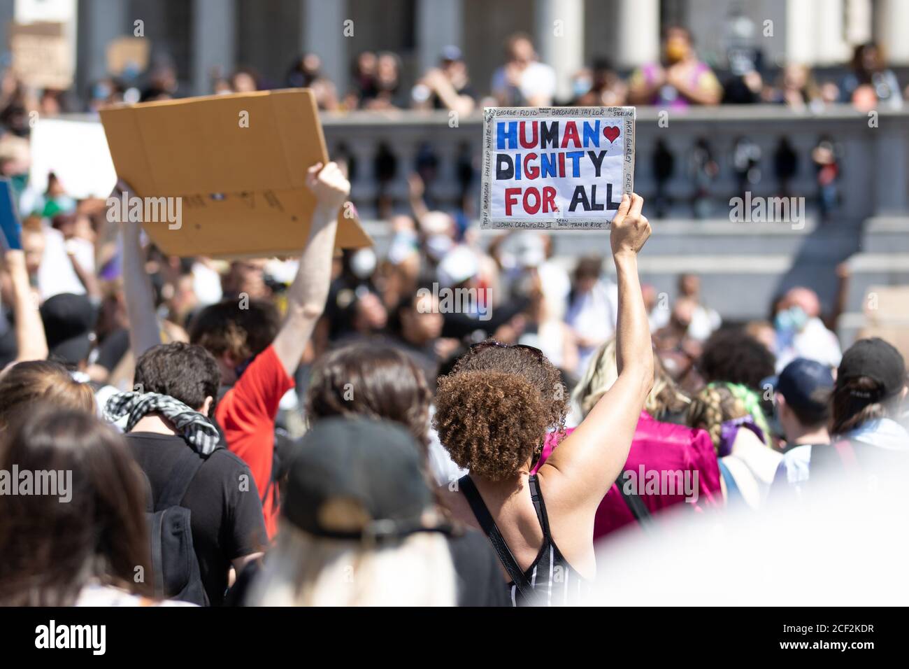 A female Black Lives Matter protestor holds a sign saying 'Human Dignity For All' at a protest in Trafalgar Square, London Stock Photo