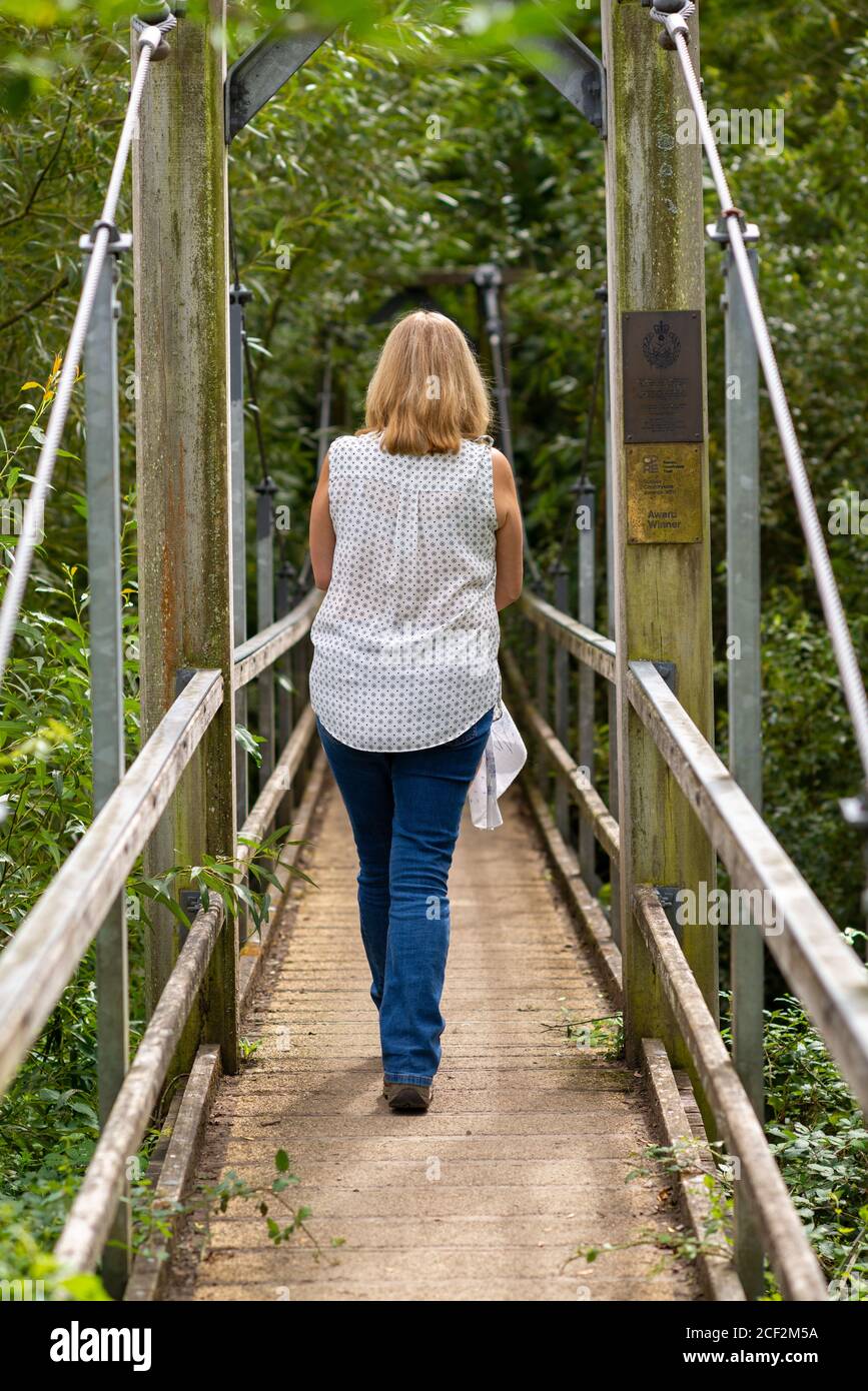 Woman walking across award winning gurkha suspension bridge, North Stoke, Amberley, South Downs National Park, West Sussex, UK Stock Photo