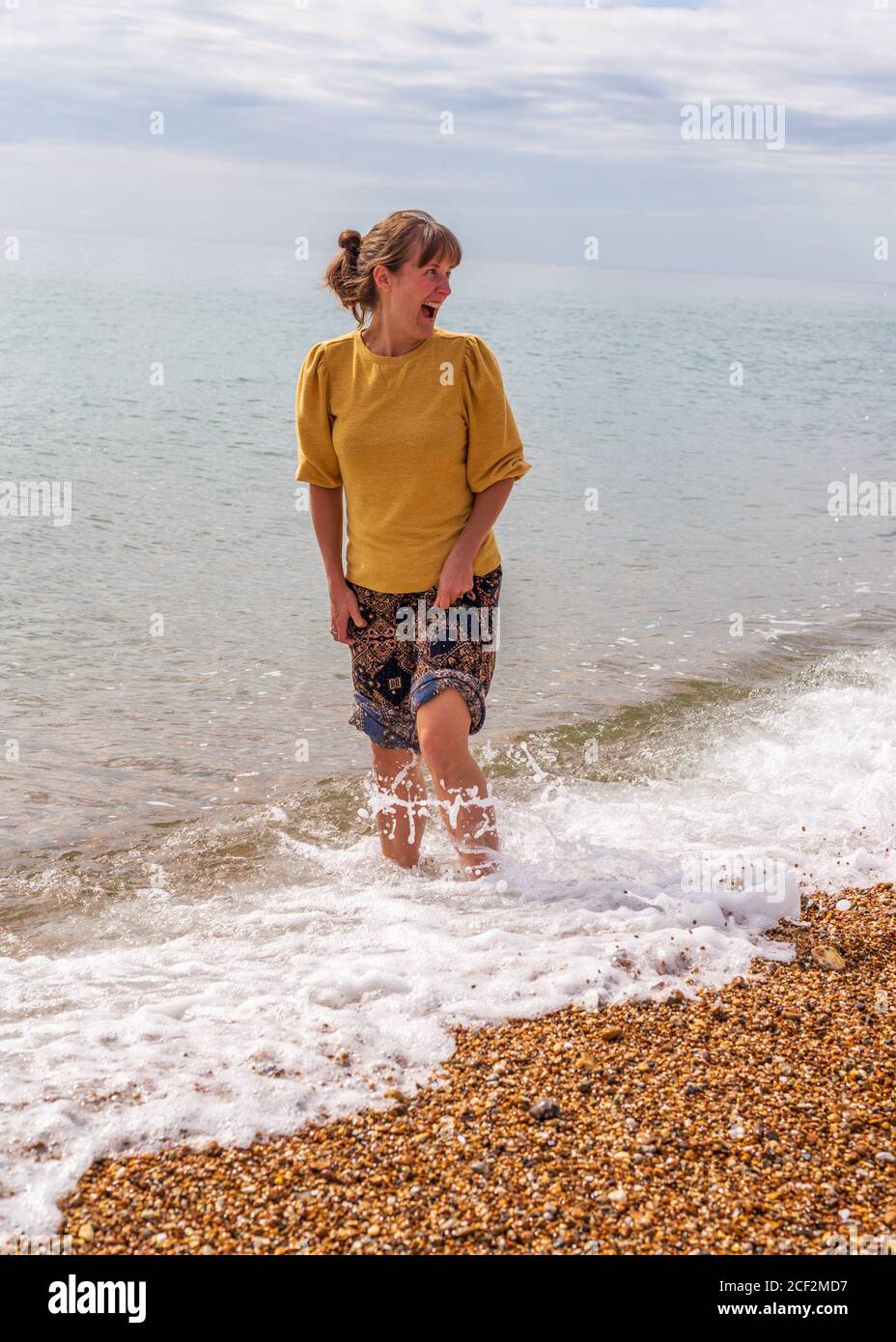 Young woman happy and smiling paddling in the sea in warm summer sunshine Stock Photo