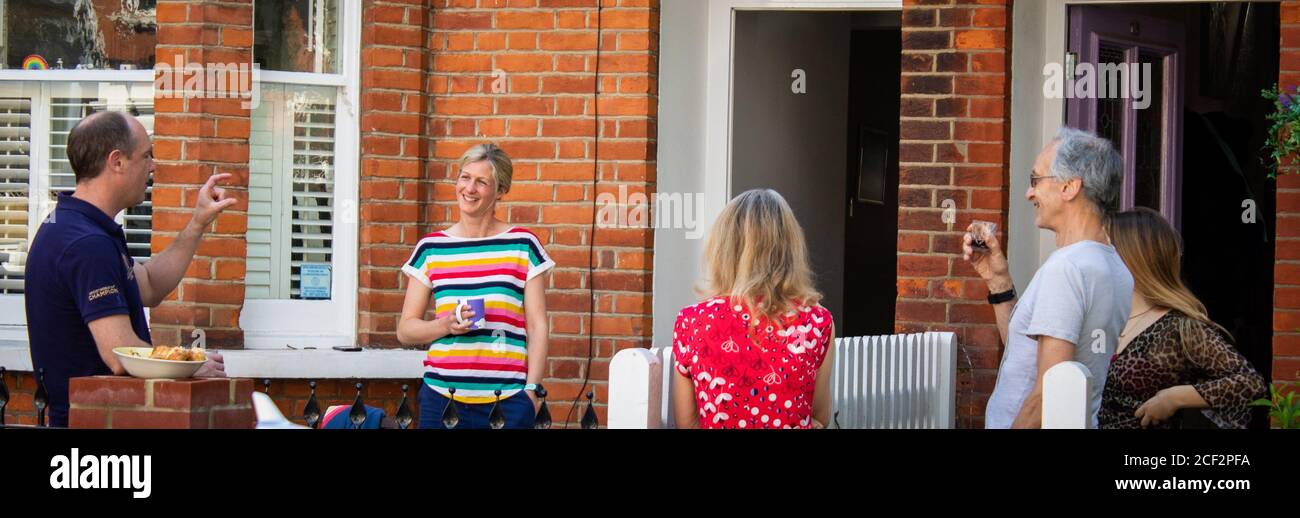 Neighbours talk to each other over the fence with drinks and snacks Stock Photo