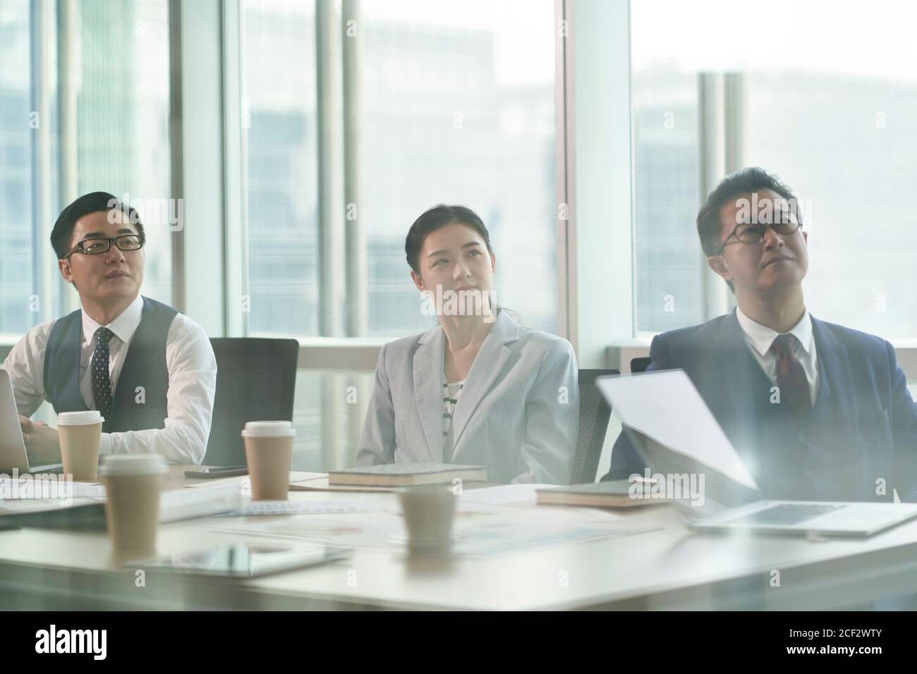 through-the-glass shot of three asian corporate executives listening with attention during business presentation Stock Photo