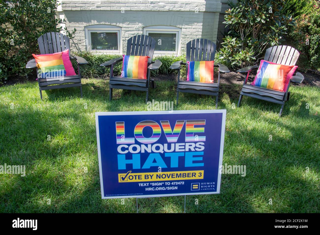 Rainbow colored seat cushions decorate lawn furniture in front of a sign reading 'Love Conquers Hate, Vote by November 3,' in the Shaw neighborhood of Stock Photo