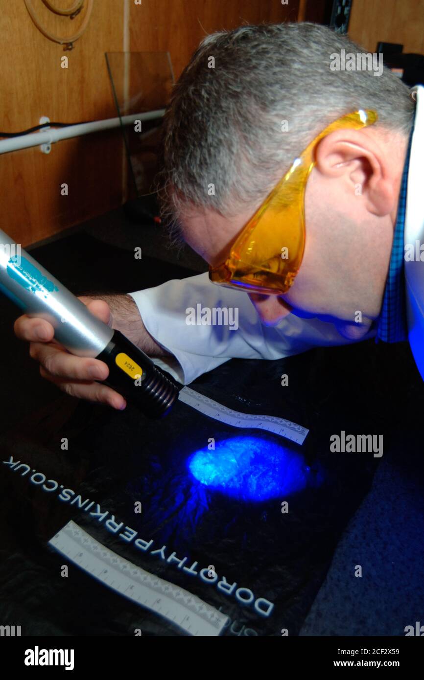 Forensic police officer searches for fingerprints on a plastic bag UK