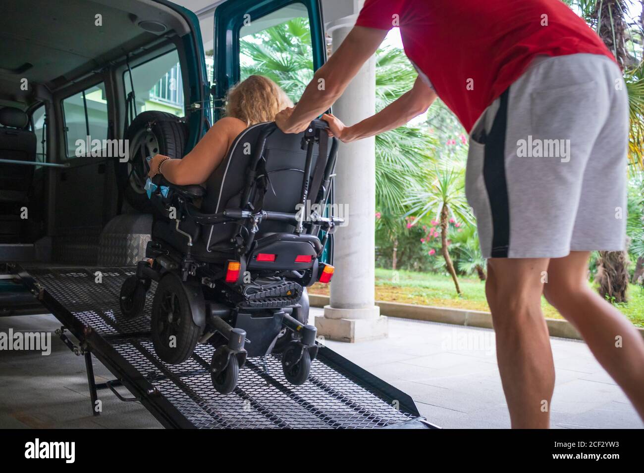 Driver assisting disabled person on wheelchair with transport using