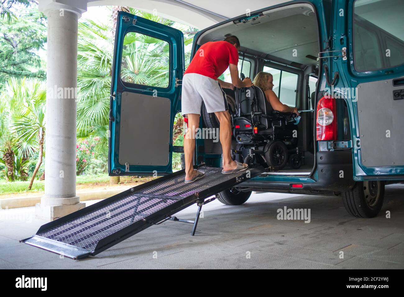 Driver assisting disabled person on wheelchair with transport using