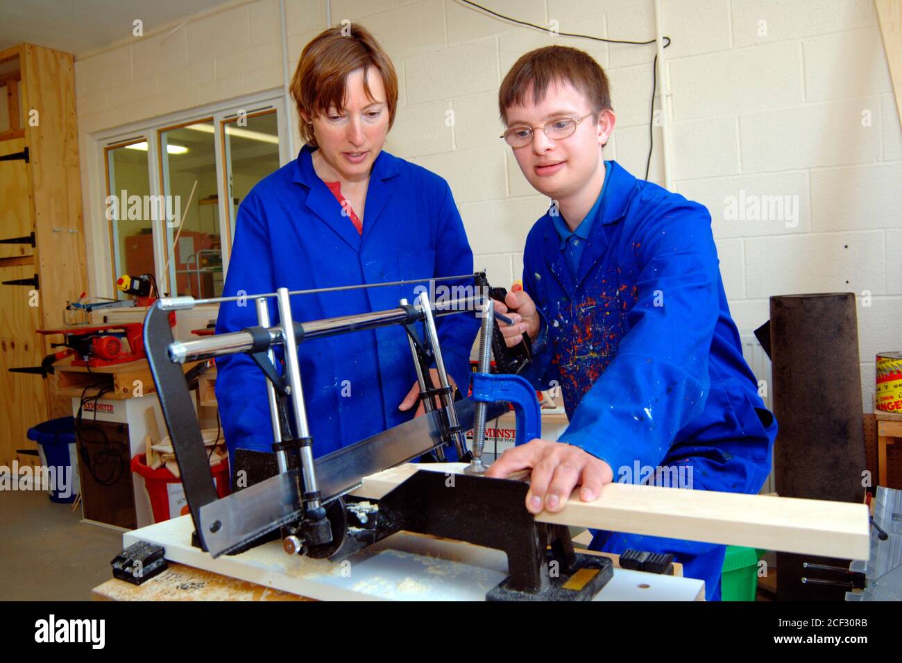 Young man with Downs Syndrome learning how to use saw at a workshop for craftspeople with learning disabilities UK Stock Photo