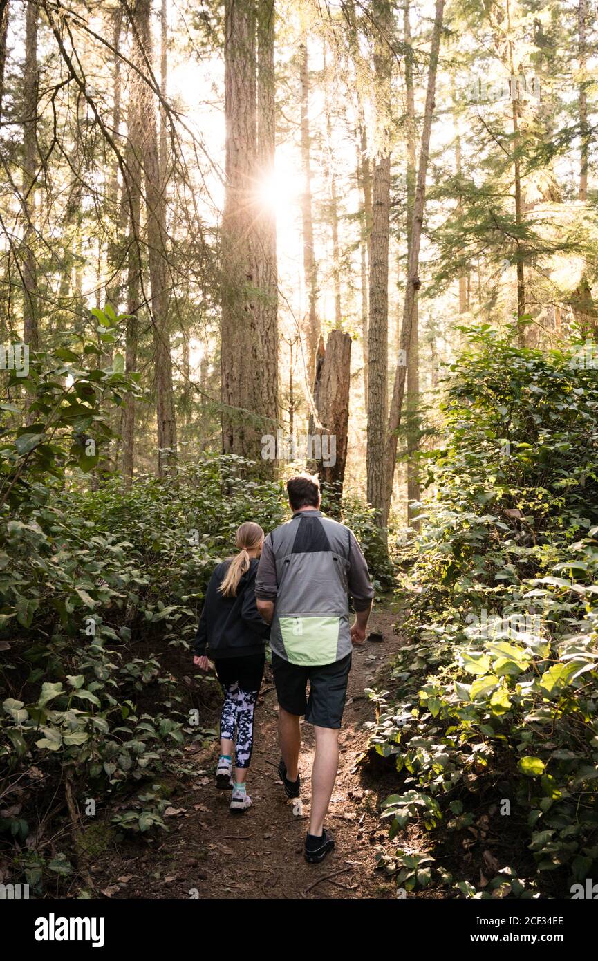 Father and Daughter Hiking on Wooded Trail on Sunny Day Stock Photo