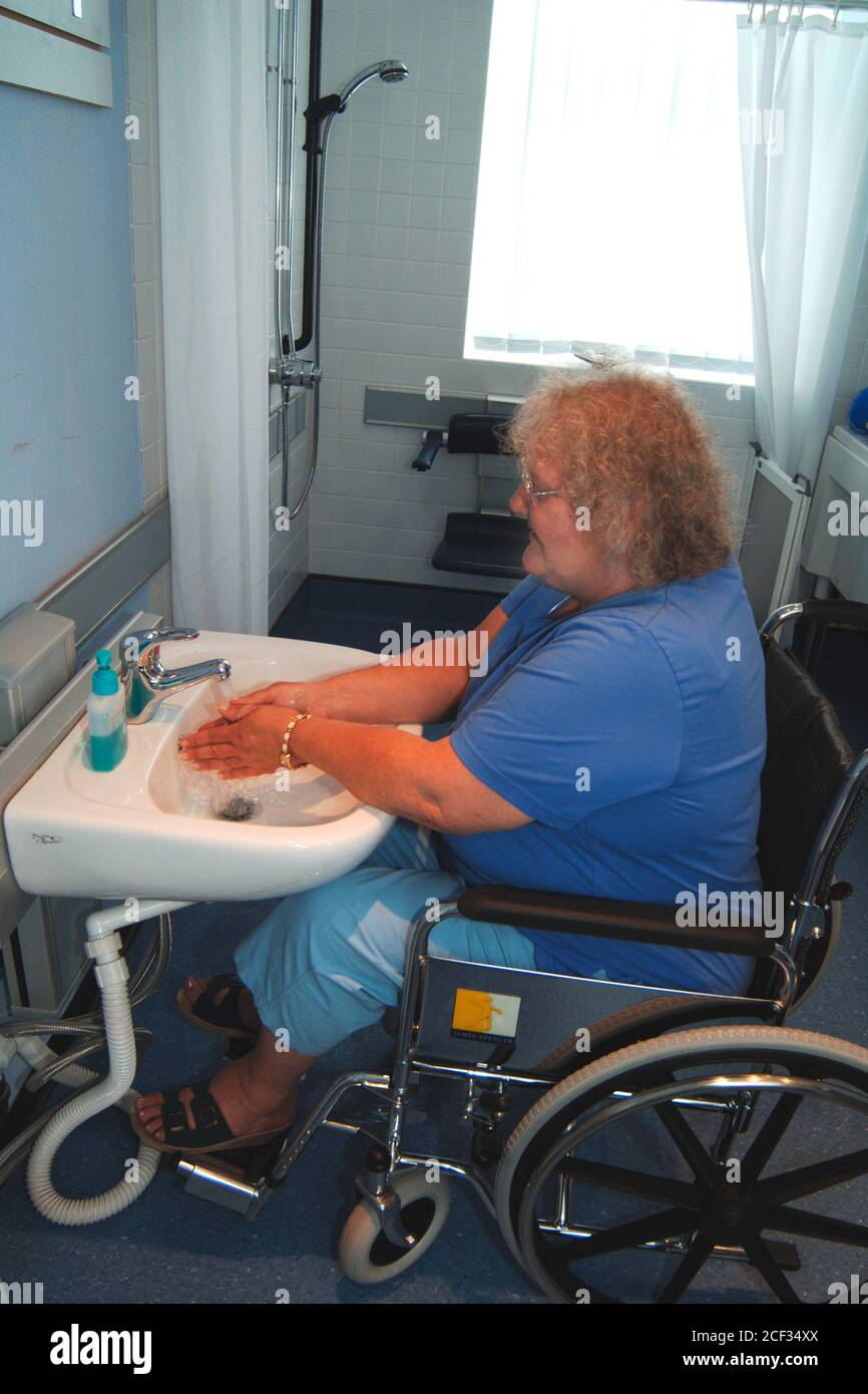 Disabled woman washing her hands in a specially adapted sink for wheelchair users UK Stock Photo