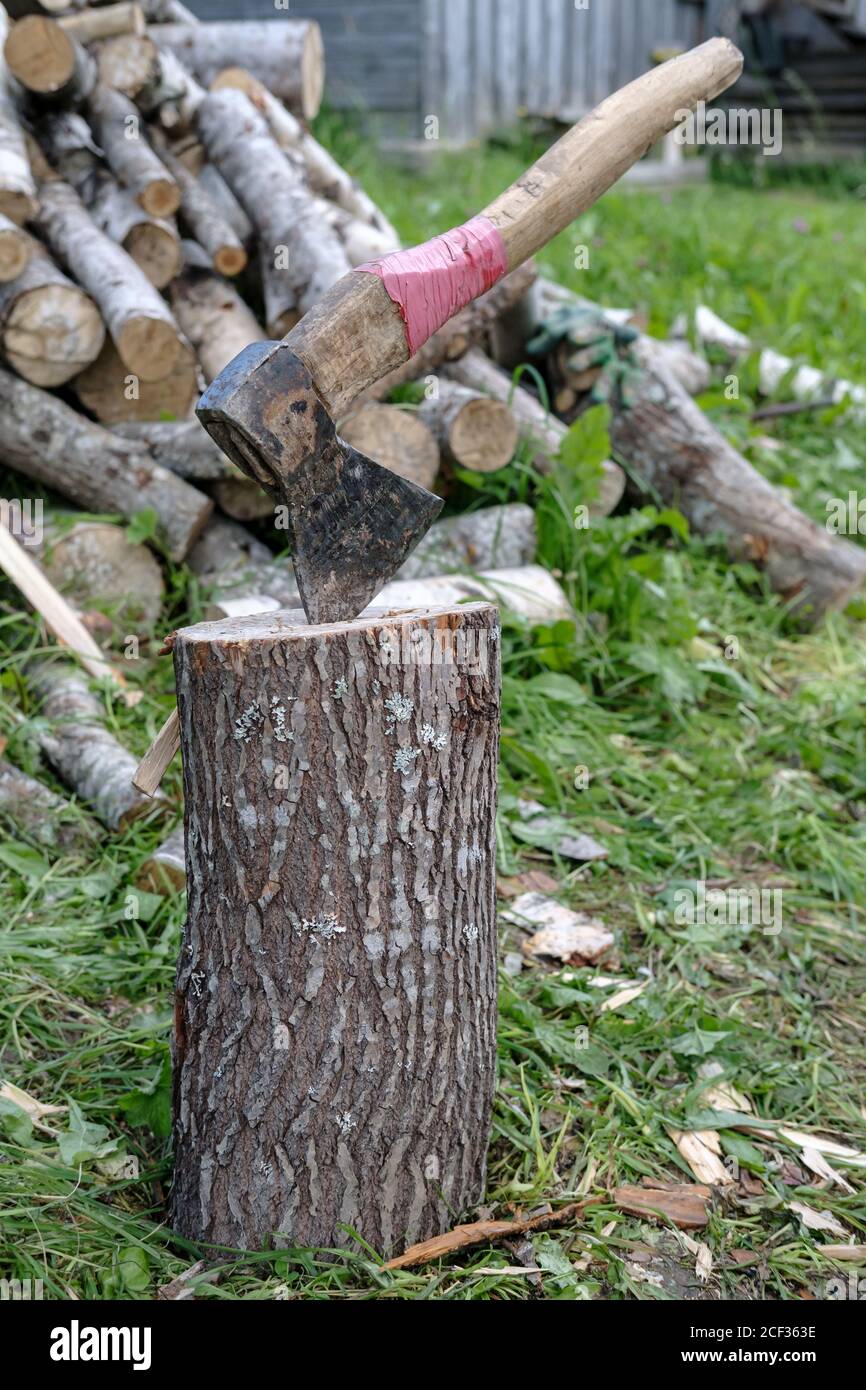Ax in a stump against the background of a pile of firewood in a village yard. Stock Photo