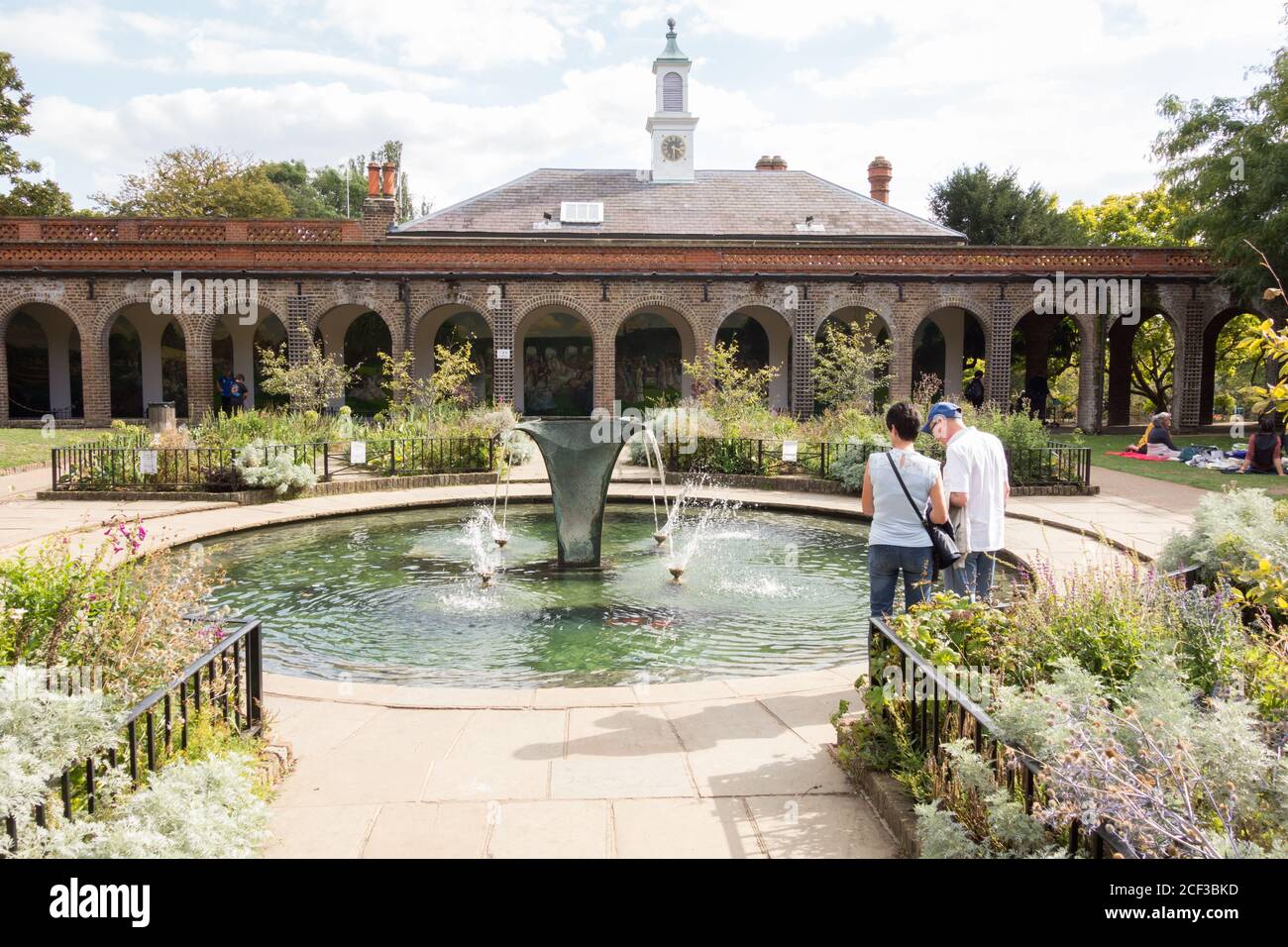A couple standing next to William Pye's Sibirica fountain gracing a pond in the Iris Garden, Holland Park, west London, UK. Stock Photo