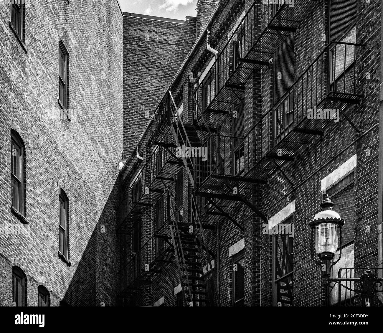 A view of intersecting lines of brick buildings in an alleyway. Three buildings meet in the middle. The building on the left is clean with spaced wind Stock Photo