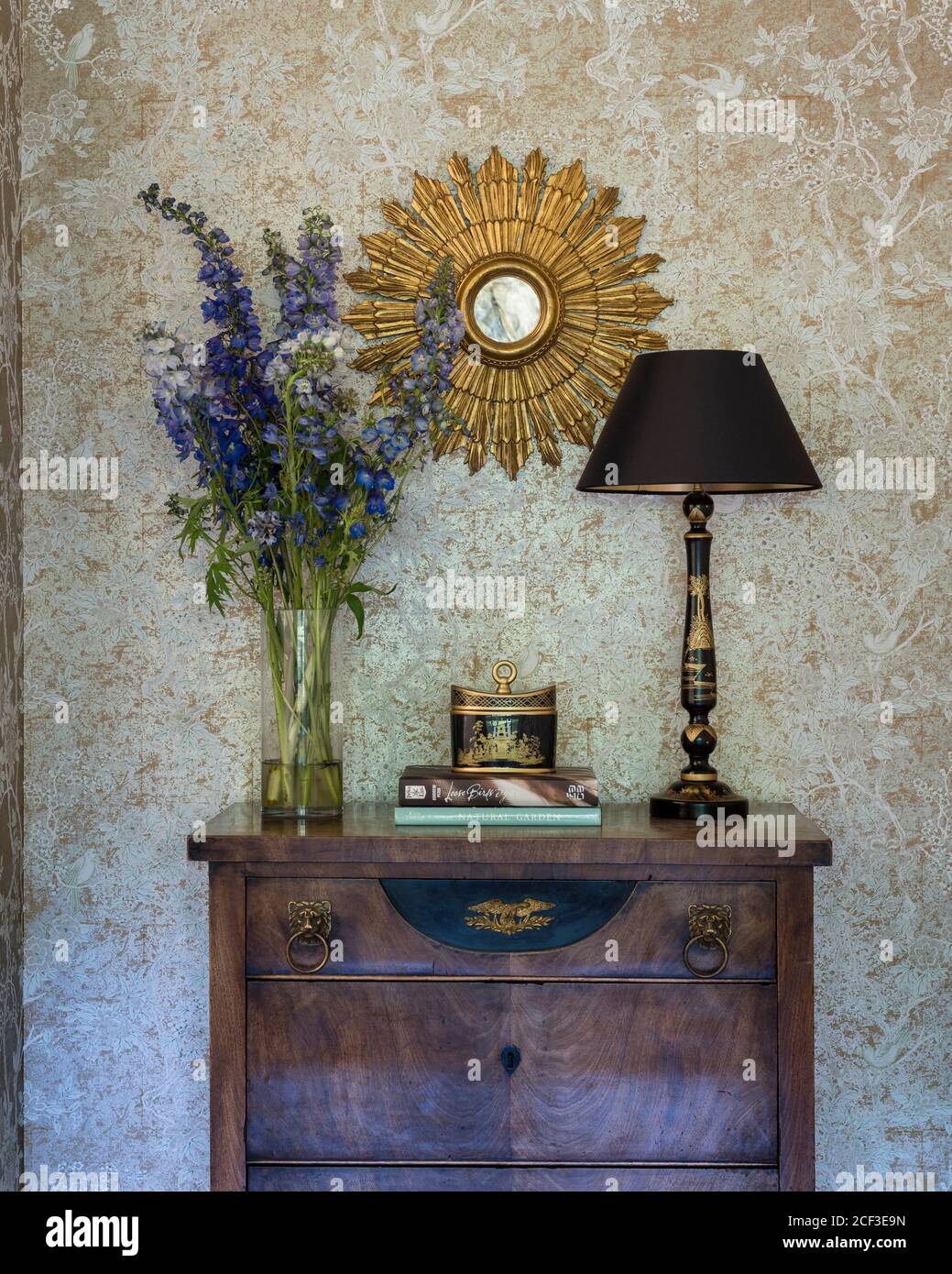 Flowers and lamp on wooden drawers below mirror Stock Photo