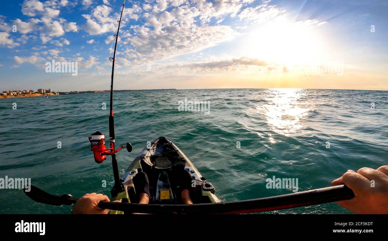 Fisherman trolling in kayak at mediterranean sea on a windy day with waves during sunset. Aquatic summer sports. Kayaker trolling and fishing at sea Stock Photo