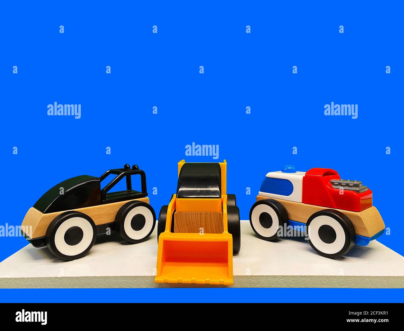 Three toy multicolored cars made of plastic and wood on a blue background Stock Photo
