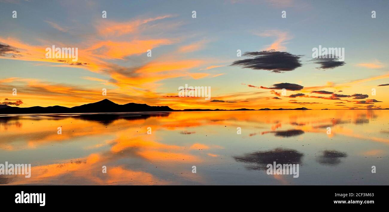 Gorgeous sunset. Orange beautiful sunset sky over salt lake in Uyuni, Bolivia. Surreal landscape of salt flats. Magic reflection of heaven in water. Stock Photo