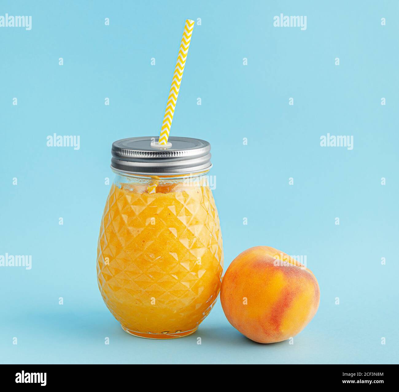 Peach smoothie jar with yellow drinking straw on blue background Stock