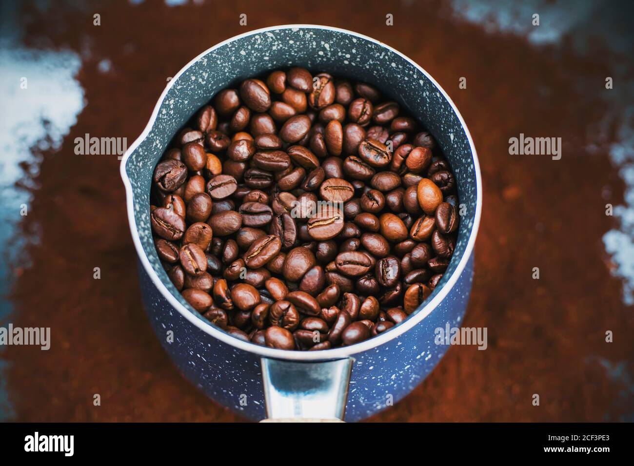 On the ground coffee is a beautiful blue cezve, which is filled with roasted coffee beans, which will then be made strong coffee. Stock Photo