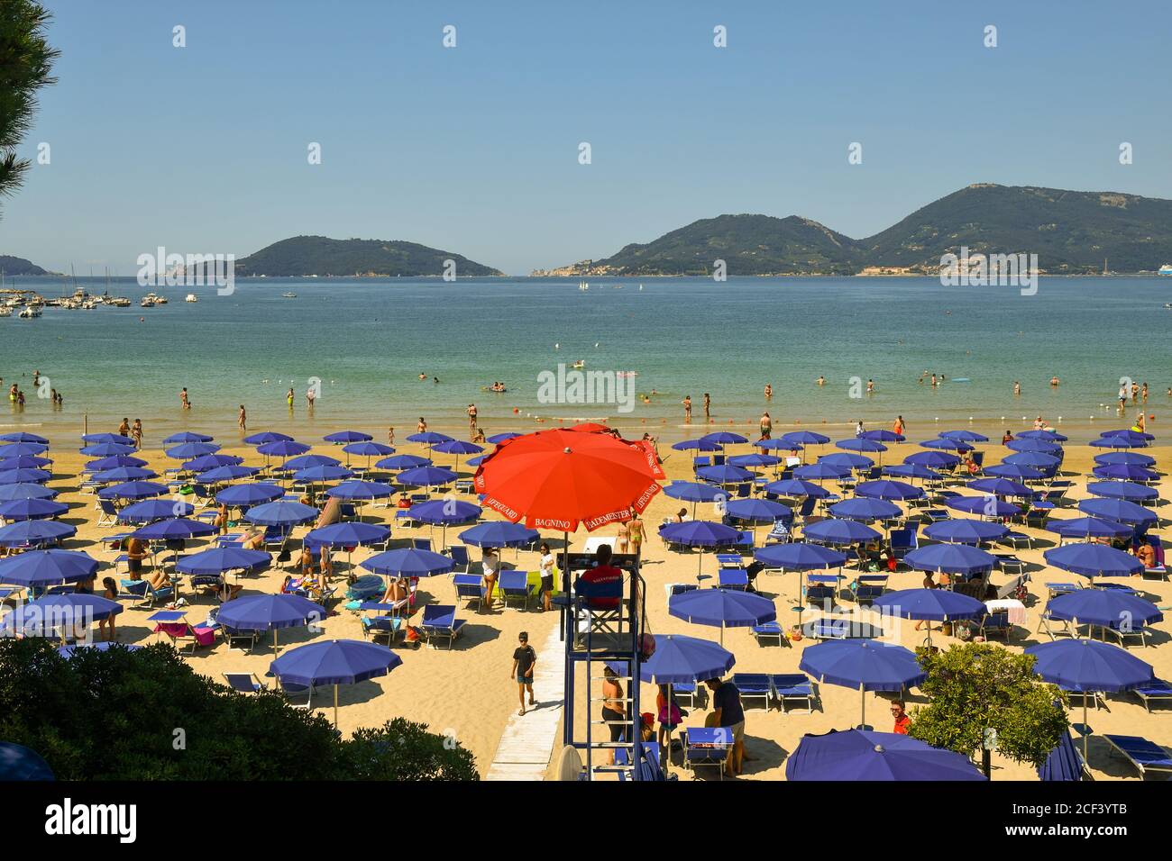 Sandy beach with lifeguard tower and rows of sun umbrellas on the shore of Gulf of Poets with Porto Venere and Palmaria Island, Lerici, Liguria, Italy Stock Photo