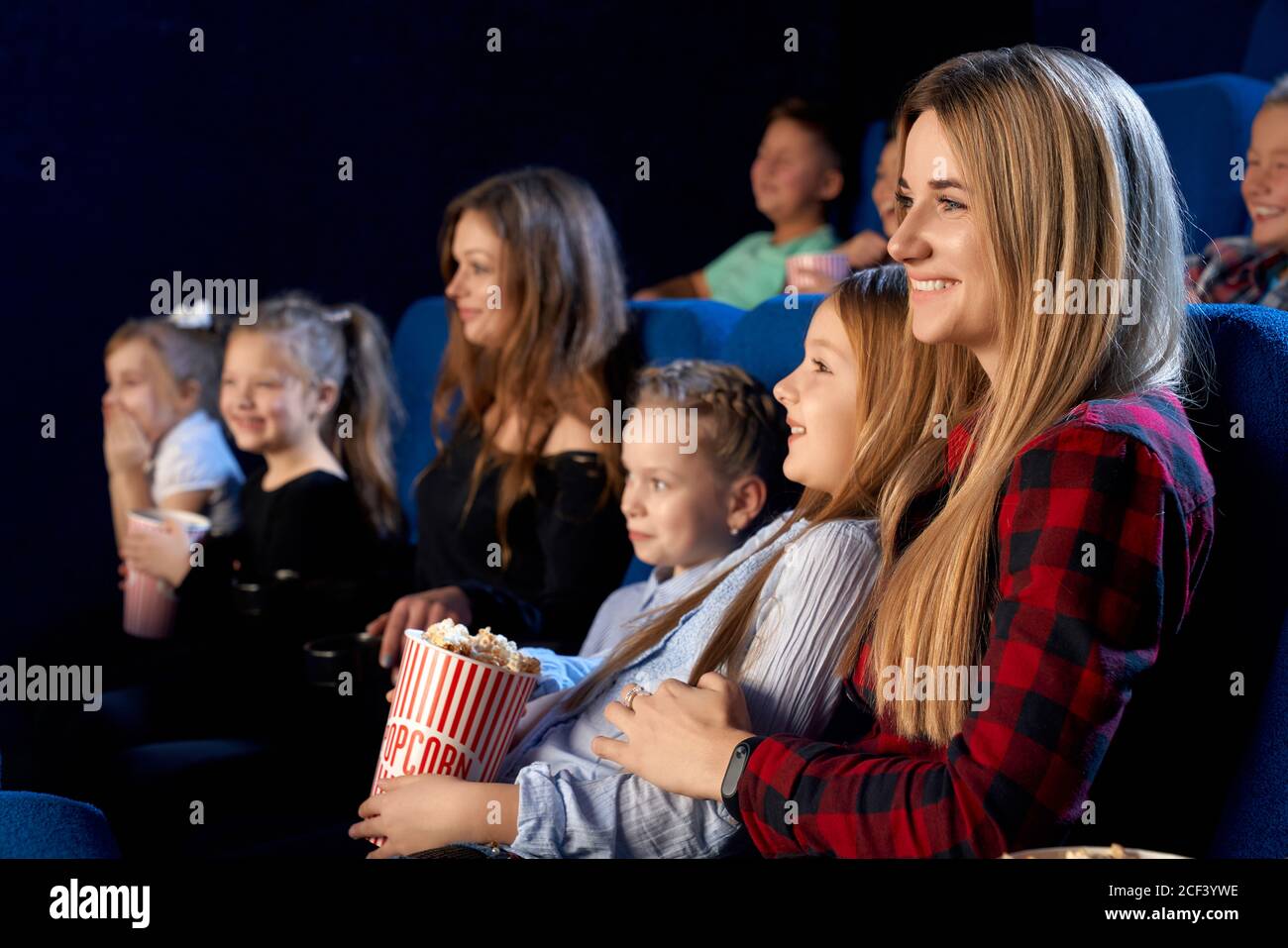 Family spending time together in cinema. Selective focus of young mother holding little daughter on knees and smiling while watching film and eating popcorn. Concept of leisure, entertainment. Stock Photo