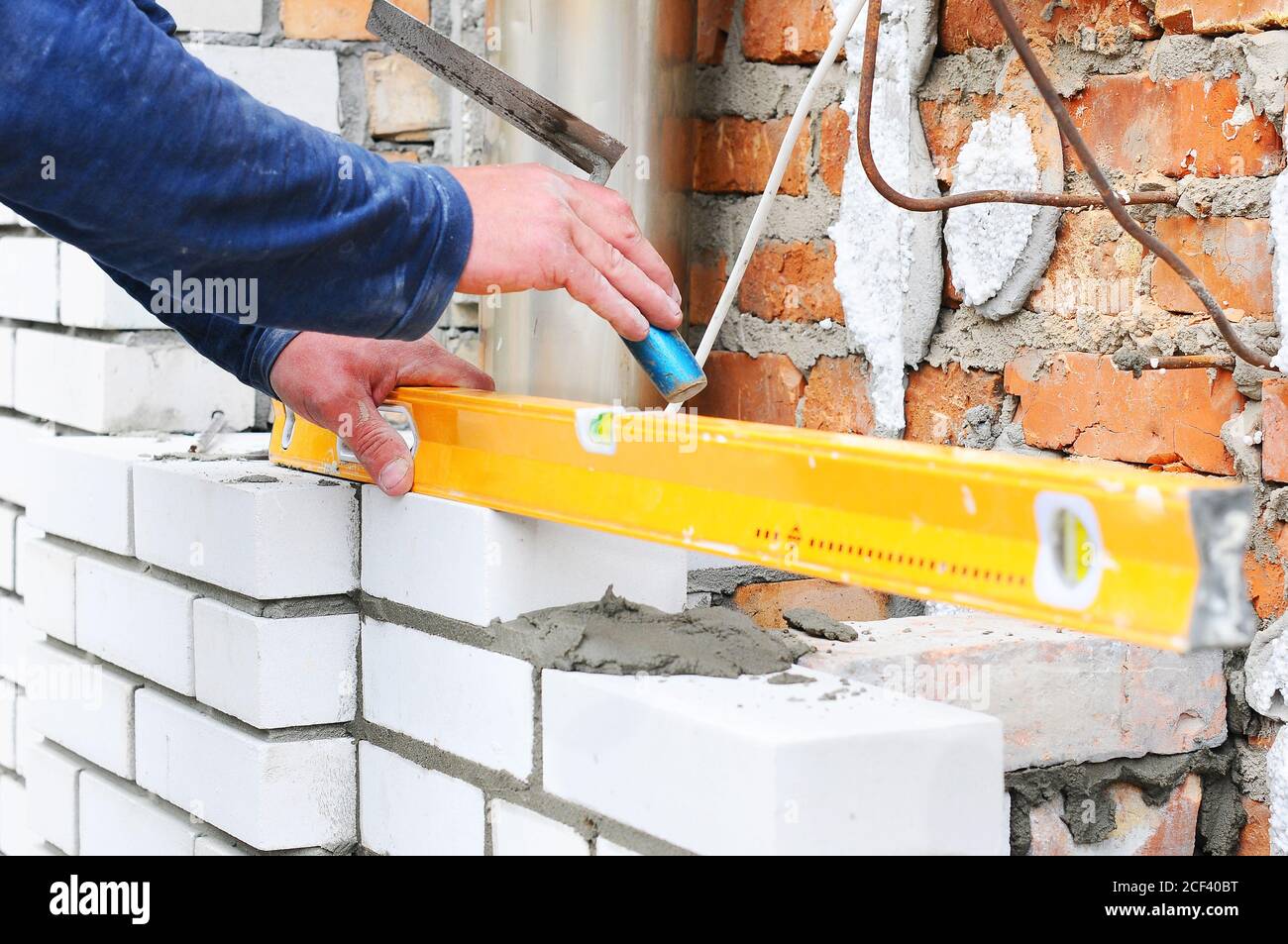 A closeup of a bricklayer worker installing white blocks and caulking