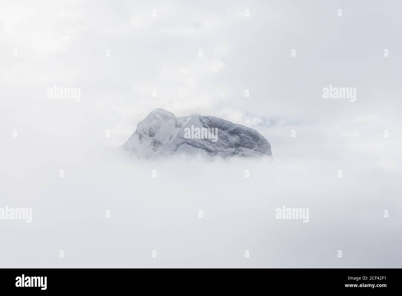 Rocky snowy mountain high in cloudy sky in foggy white day Stock Photo