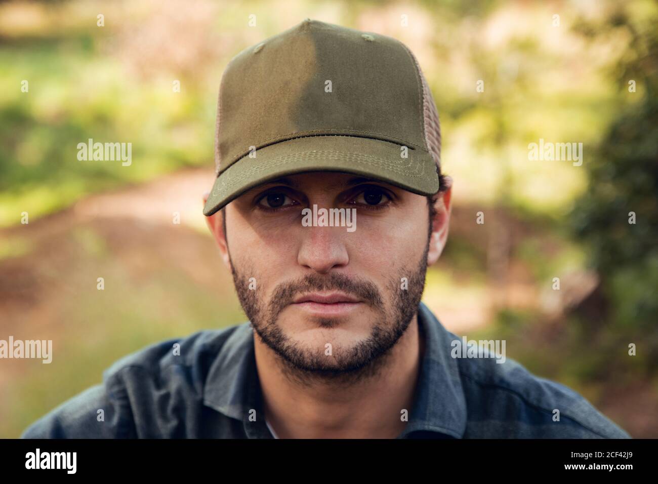 Portrait of handsome brunet man in checkered shirt and baseball cap  standing in nature background looking at camera Stock Photo - Alamy
